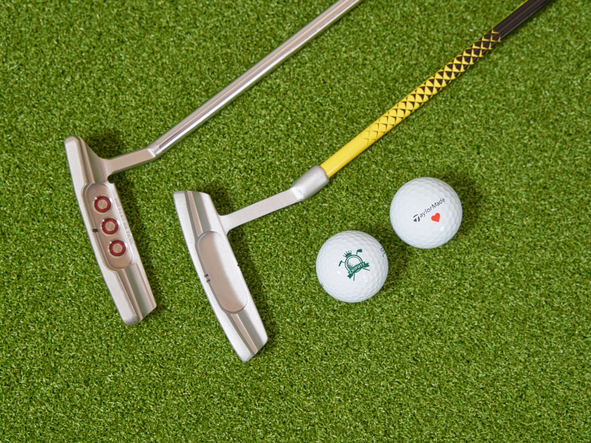 A Scotty Cameron putter alongside a kid’s putter on a Chiputt mat, with a Chiputt branded Titleist Pro V1 golf ball and a Taylormade TP5 golf ball marked with a red heart, symbolizing family bonding through golf for both adults and children.