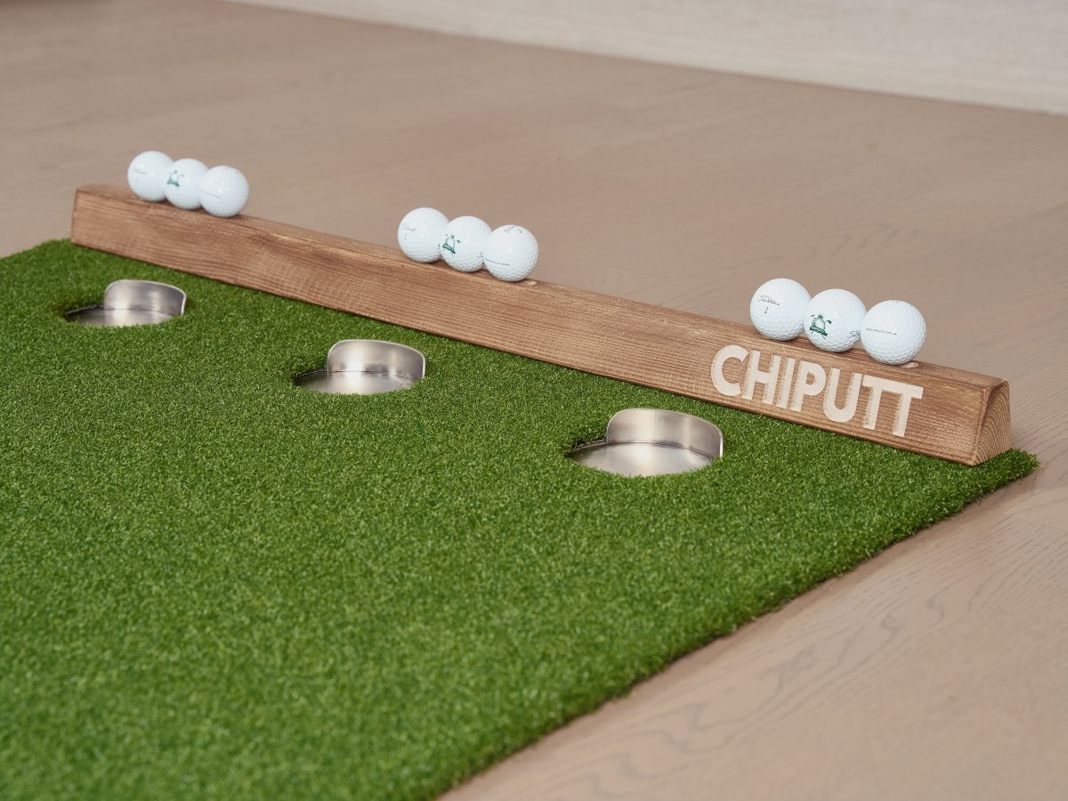 Chiputt putting mat close-up showing 3 hole cups with back lips, wooden backstop, and 9 golf balls in aesthetic detail