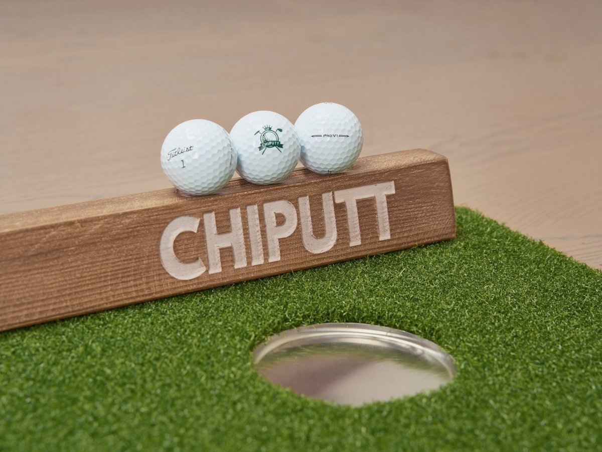 Chiputt putting mat branded Titleist Pro V1 golf balls on wooden backstop with realistic hole cup detail