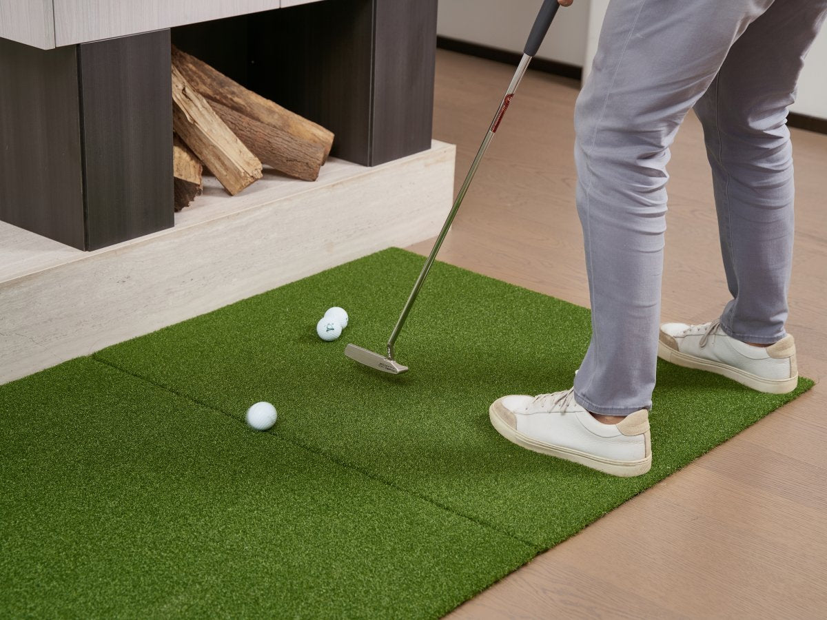 Golfer putting on connected Chiputt chipping mat extension with ball rolling seamlessly across seam to putting mat in living room