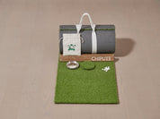 This image showcases the contents of a Chiputt mat box (1.5 feet wide compact option), including the rolled-up mat with mat strap, wooden backstop, one stainless steel hole cup, one hole cut-out, one Chiputt logo accessory pouch, and two sets of white distance markers. This setup is for the 1.5 feet width Chiputt mat compact option, ideal for golfers seeking a realistic, versatile practice experience at home with limited space.