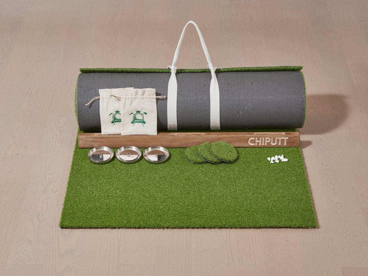 This image showcases the contents of a Chiputt mat box (3 feet wide option), including the rolled-up mat with mat strap, wooden backstop, three stainless steel hole cups, three hole cut-outs, Chiputt logo accessory pouches, and two sets of white distance markers. This setup is for the 3 feet width Chiputt mat option, ideal for golfers seeking a realistic, versatile practice experience at home.