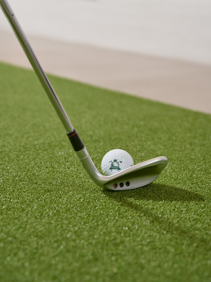 Close-up of a golf wedge ready to hit a Chiputt branded golf ball on Chiputt putting mat, demonstrating precision and control for indoor golf chipping practice.