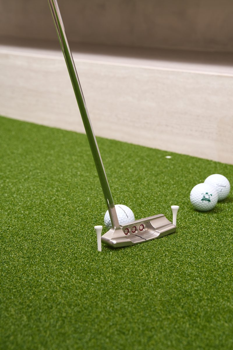 Scotty Cameron Newport putter addressing a Titleist ball through a tee gate on the Chiputt mat with two Chiputt-branded practice balls in the background, vertical