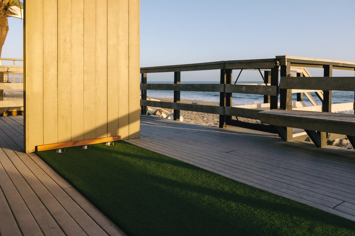 Chiputt putting mat on a beach house deck in California, facing the sand and ocean with the wooden backstop visible.