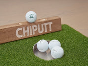 Chiputt putting mat showing successful putting with back lip cup, 3 Chiputt-branded Titleist Pro V1 balls in hole and 1 on backstop