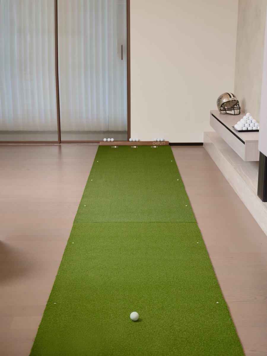 Indoor golf practice setup with Chiputt mat and extender, displaying a ball on the extender, lengthening short game practice distance, with a backdrop of a modern living area.