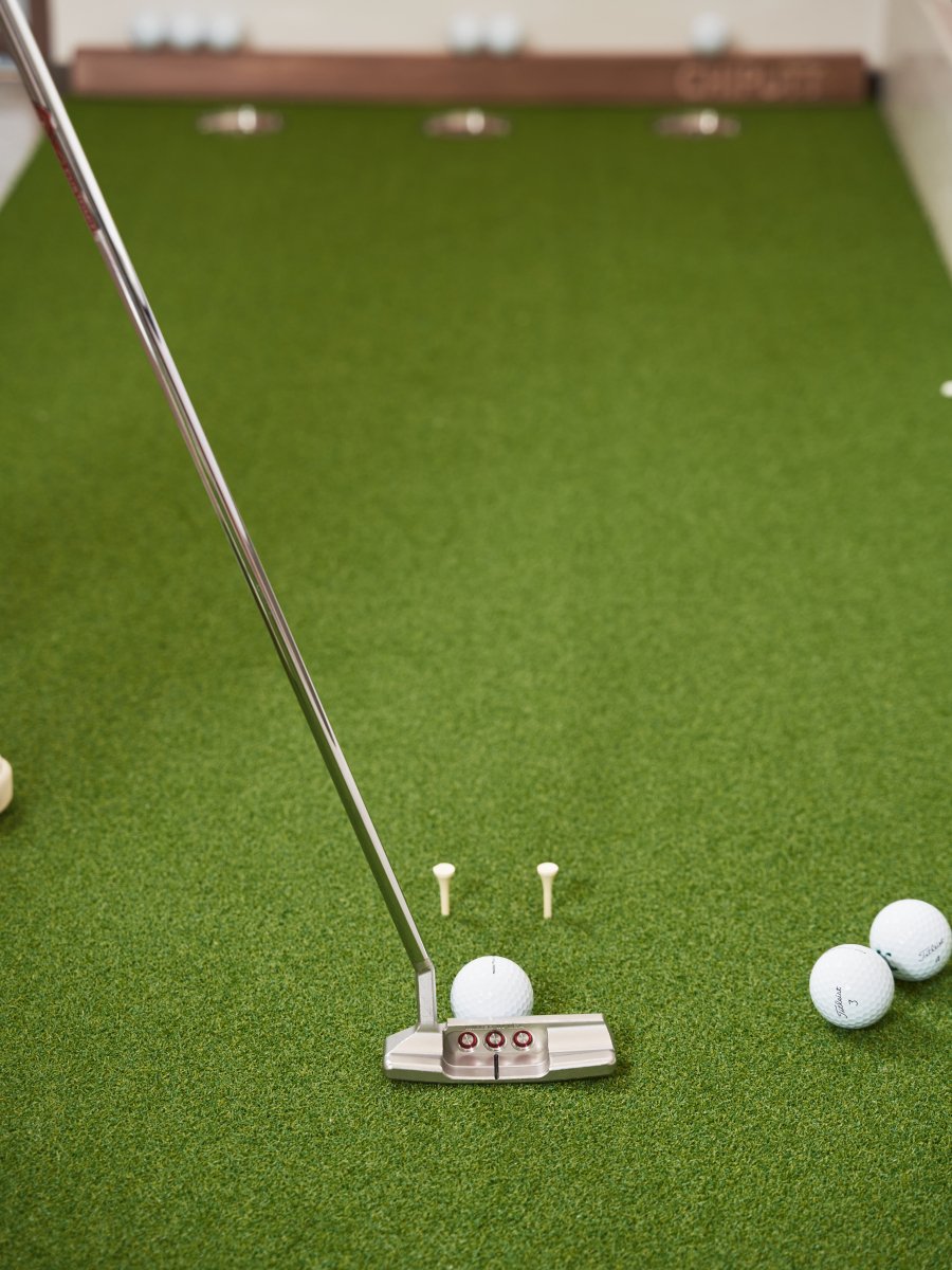 The golfer is performing a tee gate putting drill on the Chiputt mat with a Scotty Cameron putter and Titleist Pro V1 golf balls.