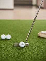 Golfer practicing putting on a Chiputt mat with a Scotty Cameron putter, targeting a Titleist Pro V1 golf ball marked with the Chiputt logo, illustrating precision putting training at home.